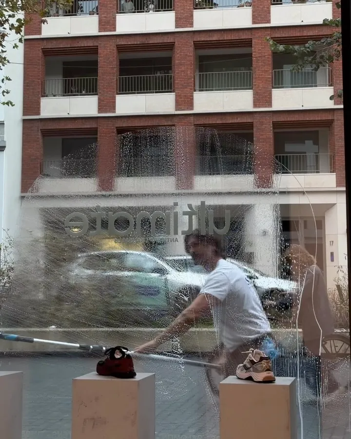 Met de wisser over een grote vitrine, de gevel aan de overkant weerspiegelt in het glas