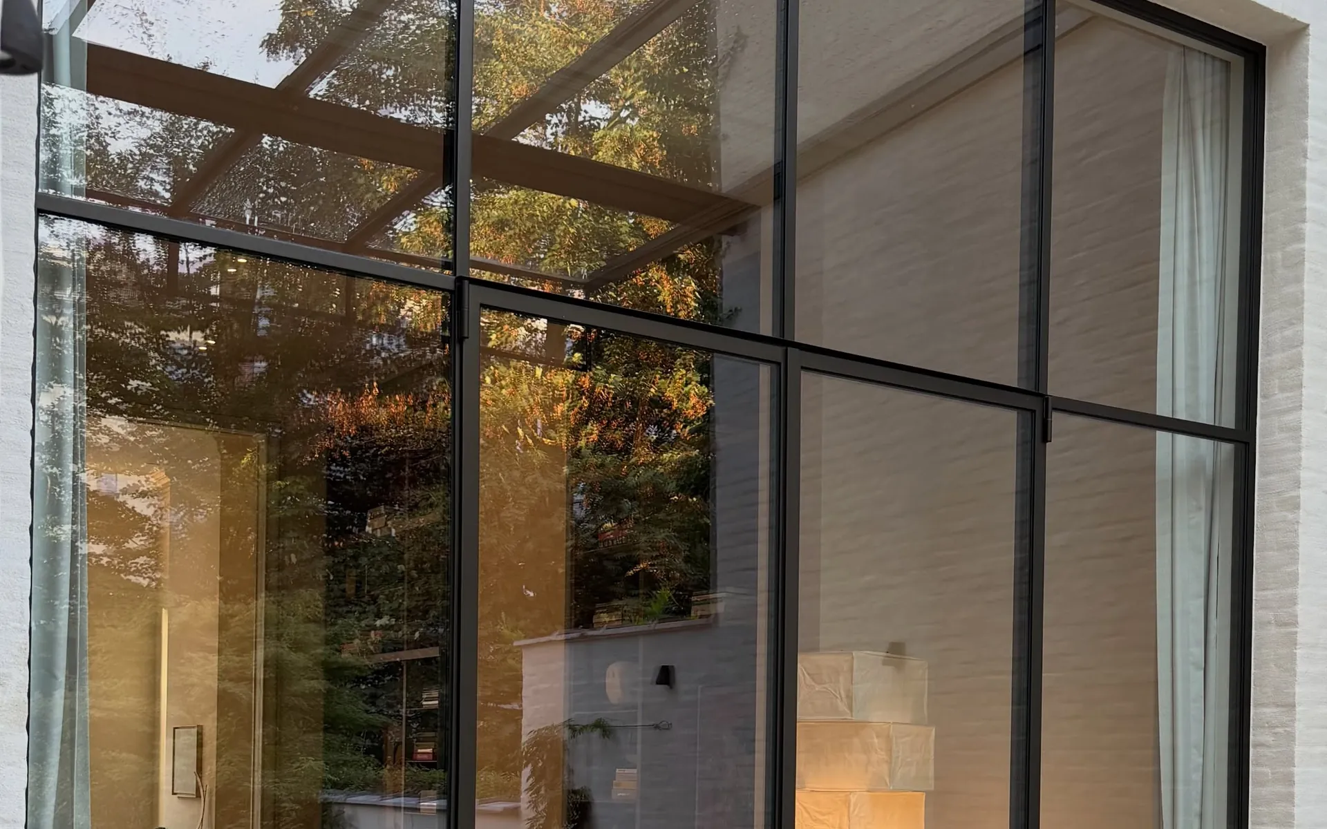 Stalen raampartij van vloer tot plafond, de tuin weerspiegeld in het heldere glas
