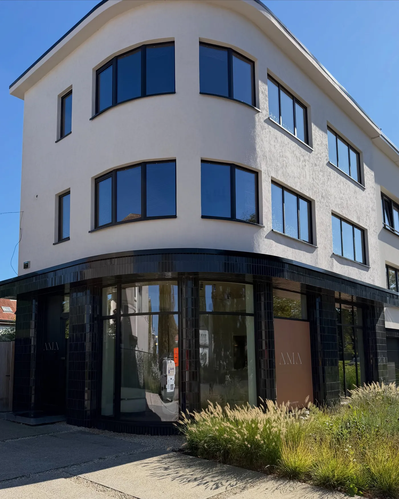 Witte hoekwoning met gebogen gevel en donkere ramen tegen een blauwe lucht